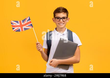 Étudiez à l'étranger. Écolier souriant dans des lunettes tenant un ordinateur portable et drapeau britannique Banque D'Images