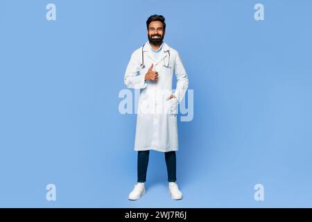 Médecin indien donnant les pouces vers le haut sur fond bleu Banque D'Images