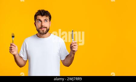 Hungry Guy tient couteau et fourchette prêt à savourer le repas, studio Banque D'Images