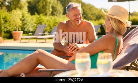 Couple senior en vacances portant des costumes de bain relaxant près de la piscine de l'hôtel Banque D'Images
