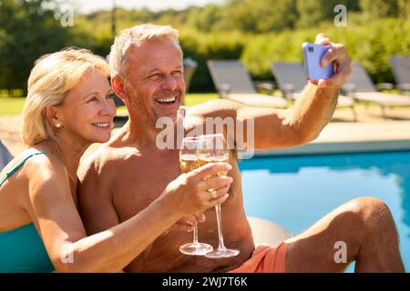 Couple senior en vacances posant pour Selfie boire du champagne relaxant près de la piscine de l'hôtel Banque D'Images