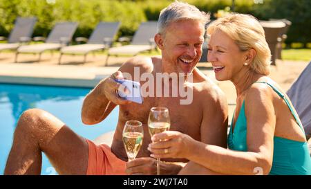 Couple senior en vacances posant pour Selfie boire du champagne relaxant près de la piscine de l'hôtel Banque D'Images