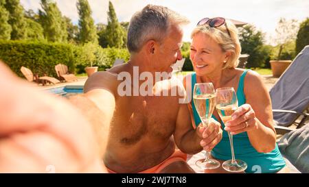 Plan POV d'un couple senior en vacances posant pour Selfie boire du champagne relaxant au bord de la piscine Banque D'Images