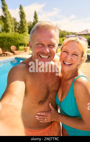 Plan POV d'un couple senior en vacances posant pour Selfie portant des costumes de natation près de la piscine Banque D'Images