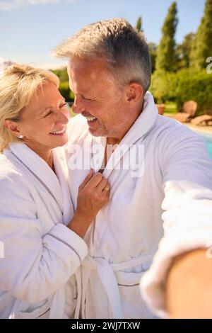 Plan POV d'un couple senior en peignoirs à l'extérieur près de la piscine le jour du spa Banque D'Images