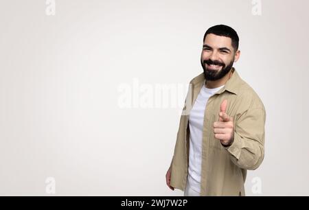 Sourire confiant beau jeune latin jeune avec une barbe dans le doigt de point décontracté à la caméra Banque D'Images