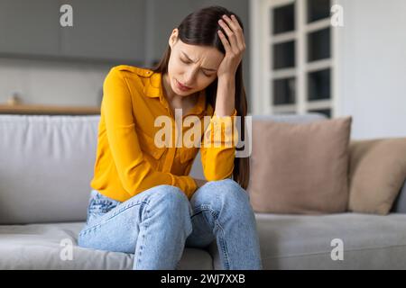 Jeune femme stressée avec mal de tête assise sur le canapé Banque D'Images