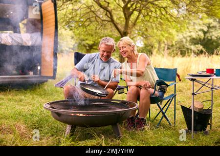 Couple senior Camping à la campagne avec RV Cooking Bacon et œufs pour le petit déjeuner en plein air sur le feu Banque D'Images