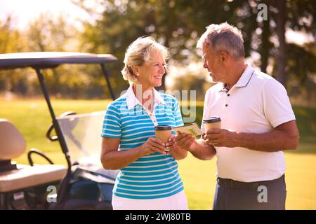 Couple senior avec buggy sur le parcours de golf marquant la carte de score ensemble Banque D'Images