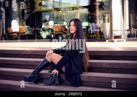 Une femme élégante portant une tenue confortable et des bottes est assise sur les marches extérieures Banque D'Images