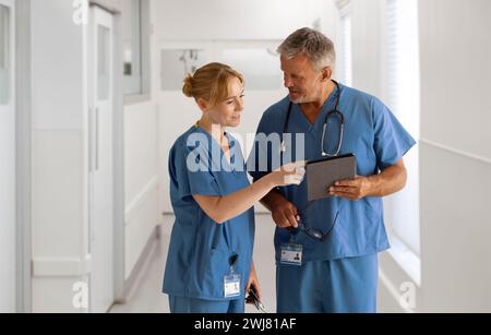 Équipe médicale portant des gommages se réunissant dans le couloir de l'hôpital en regardant la tablette numérique ensemble Banque D'Images