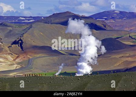 Les randonneurs traversent des paysages arides et volcaniques sur lesquels dérivent les panaches de vapeur de l'activité géothermique, Namafjall, Myvatn, Islande Banque D'Images