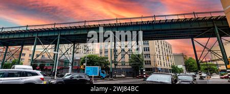 New York, USA ; 3 juin 2023 : train aérien typique et voies de tramway du Bronx, un quartier de la Big Apple, sous un ciel orange au coucher du soleil. Banque D'Images