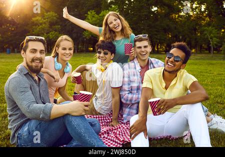 Groupe d'amis multiraciaux heureux assis ensemble sur une couverture appréciant au pique-nique dans le parc Banque D'Images