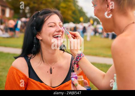 Deux amies riantes décorant des visages avec des paillettes au Festival de musique d'été Banque D'Images