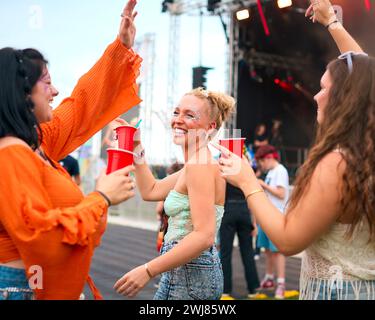 Trois amies féminines portant des paillettes s'amusant au Festival de musique d'été en prenant un verre Banque D'Images