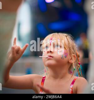 Fille assise sur les épaules de ses parents faisant un geste de main Rock and Roll au Festival de musique d'été en plein air Banque D'Images