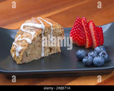 Un gros plan d'une tranche de pain aux courgettes maison avec glaçage, bleuets et une fraise tranchée sur une assiette. Banque D'Images