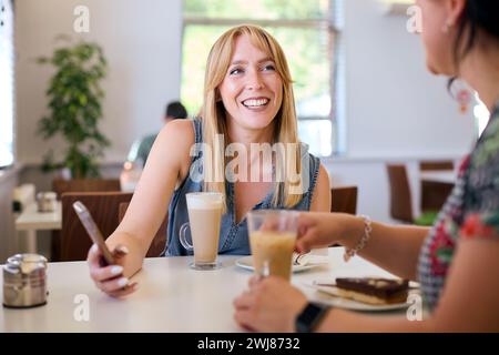 Deux amis féminins se réunissant dans le café-restaurant regardant téléphone portable ensemble Banque D'Images