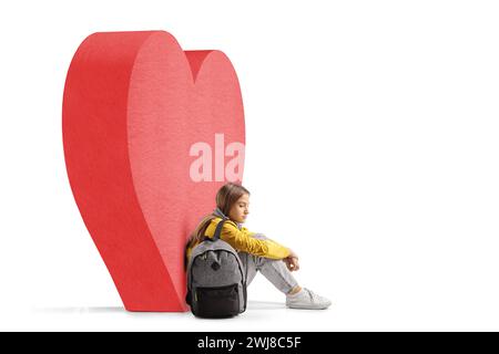 Adolescente Diasppointer assise sur le sol à côté d'un cœur rouge isolé sur fond blanc Banque D'Images