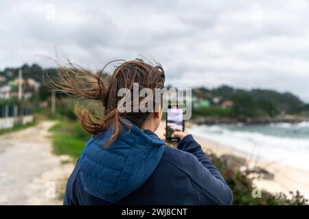 Femme prenant une photo avec son smartphone à la plage par un jour nuageux Banque D'Images