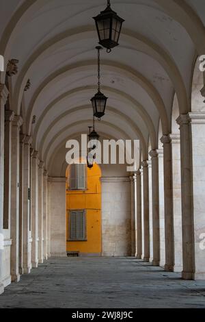 Passage avec des colonnes antiques dans la vieille ville de Bergame avec une façade orange antique et fenêtres en bois et volets en bois en arrière-plan. Banque D'Images