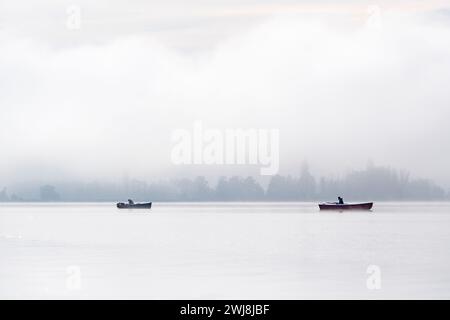 Deux bateaux de pêcheurs tôt le matin sur un lac couvert de brouillard. Banque D'Images
