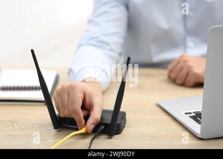 Homme insérant le câble dans le routeur Wi-Fi à la table en bois à l'intérieur, gros plan Banque D'Images