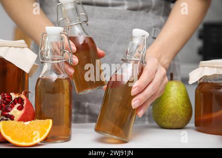 Femme prenant des bouteilles de kombucha fermenté à table blanche, gros plan Banque D'Images