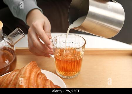 Femme versant du lait dans la tasse avec du thé aromatique à la table à l'intérieur, gros plan Banque D'Images