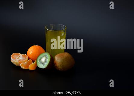 Un grand verre d'un mélange de jus de fruits sur fond noir, mandarine mûre et kiwi. Gros plan. Banque D'Images