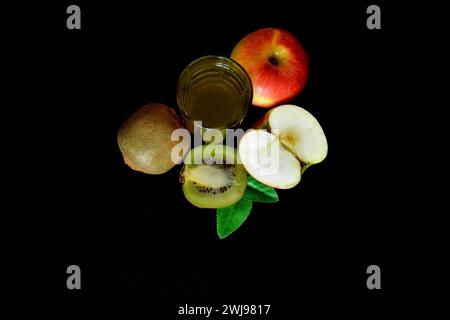 Un grand verre d'un mélange de jus de fruits sur fond noir, une pomme rouge mûre et un kiwi. Vue de dessus, pose à plat. Banque D'Images