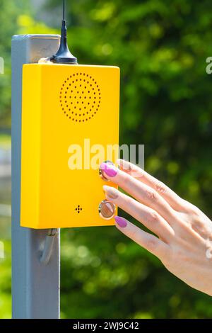 femme appuie son doigt sur le bouton d'une radio de rue .talkie-walkie stationnaire jaune dans le parc, de près. radio fixe avec antenne. Q élevé Banque D'Images