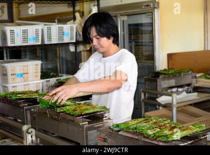 Un homme griller Otak-Otak un gâteau de poisson d'Asie du Sud-est enveloppé dans une feuille de banane. Banque D'Images