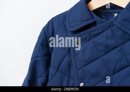 Manteau bleu matelassé pour enfants sur cintre contre mur blanc Banque D'Images