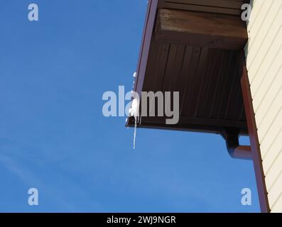 Le bord du toit avec un peu de neige et de glaçons contre le ciel bleu Banque D'Images