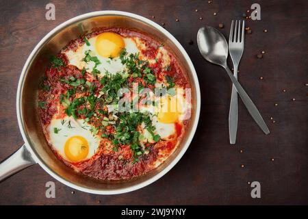 Shakshuka savoureux et sain, omelette du Moyen-Orient dans une poêle. Délicieux œufs brouillés cuits dans une sauce tomate-poivre épicée sur une languette en bois rugueuse Banque D'Images