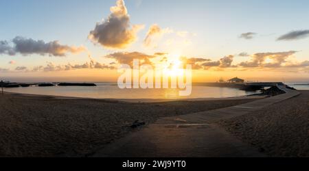 L'aube se brise sur la plage de la Guirra, Caleta de Fuste, projetant une lueur dorée paisible sur les eaux tranquilles de Fuerteventura Banque D'Images