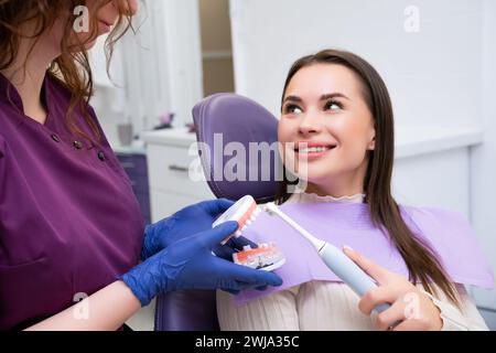 Professionnel dentaire explique à la patiente comment se brosser les dents correctement en clinique. Les dentistes utilisent le modèle dentaire de mâchoire humaine pour plus de clarté Banque D'Images