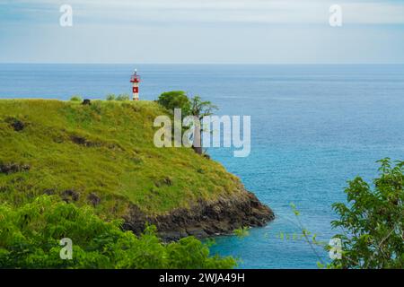 Un phare serein se trouve au sommet d'une falaise verdoyante surplombant les eaux Azur de la côte nord, avec un arbre solitaire accentuant la scène tranquille. Banque D'Images