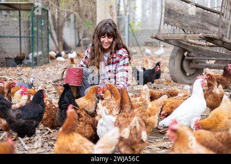 Heureuse jeune femme fermière à la main nourrissant du maïs aux poulets. Bien-être animal et soins dans une ferme biologique. Banque D'Images