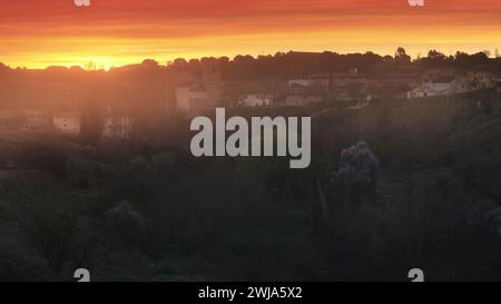 Un lever de soleil à couper le souffle illumine le ciel avec des oranges et des jaunes vibrants, projetant une lueur chaude sur la banlieue sereine en toile de fond Banque D'Images