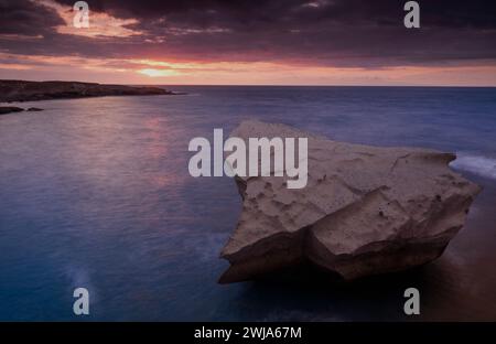 Coucher de soleil tranquille sur une mer calme avec une formation rocheuse proéminente au premier plan sous un ciel violet Banque D'Images