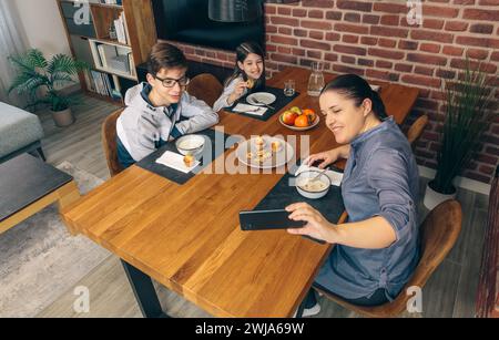 Vue d'en haut de la mère capture une photo de ses enfants prenant le petit déjeuner à la maison, avec un cadre de repas chaleureux et accueillant Banque D'Images