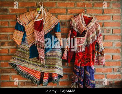 Robes vietnamiennes traditionnelles multicolores avec tissu lumineux et motifs placés contre le mur de briques avec cintre Banque D'Images