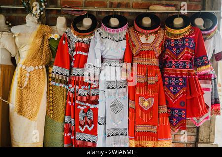 Robes vietnamiennes traditionnelles multicolores avec tissu lumineux et motifs placés contre le mur de briques avec cintre Banque D'Images