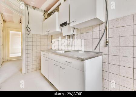 Une cuisine lumineuse et vide avec des murs inachevés, des armoires blanches et une grande fenêtre permettant la lumière naturelle. Banque D'Images