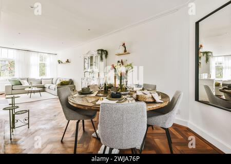 Une salle à manger élégamment décorée avec une table ronde en bois, des chaises modernes et un espace de vie élégant en arrière-plan. Banque D'Images