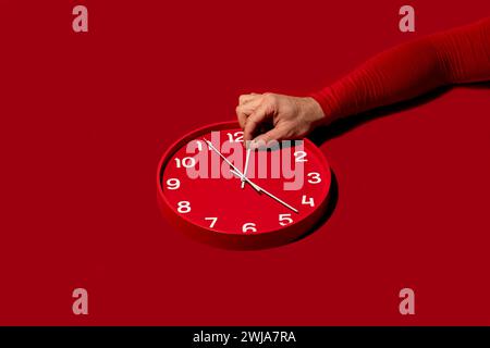 Une aiguille déplaçant l'aiguille des minutes d'une horloge murale rouge moderne sur un fond rouge assorti Banque D'Images