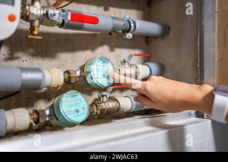 Le doigt d'une femme pointe vers les compteurs d'eau de consommation d'eau froide et chaude dans de vrais appartements, en Europe Banque D'Images